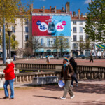 Toile publicitaire SNCF vue de face et de loin de jour à Lyon avec quelques passants.