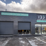 Vue d'ensemble du déploiement multi-sites 123 Pare-Brise à Tourville avec panneau logo au-dessus de l'entrée et panneau baseline horizontal.