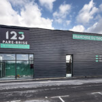 Entrée de l'accueil 123 Pare-Brise à Tourville avec panneau logo, baseline et textes en lettrages découpés pour un déploiement multi-sites réussi.