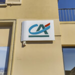 Signalétique d'agence bancaire à Buxy de jour, avec une enseigne en angle et une enseigne drapeau.