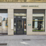 Vue de rue de la signalétique d'agence bancaire à Lyon Ainay, avec enseigne drapeau, lettrage et vitrophanie paysage.