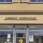 Entrée avec signalétique d'agence bancaire à Buxy, comprenant un lettrage lumineux sur lisse et des vitrophanies.