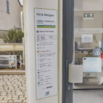 Détail de la signalétique d'agence bancaire à Villié Morgon, montrant un panneau d'horaires en tôle aluminium laqué sur le mur de l'entrée.