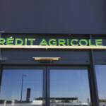 Zoom sur l'enseigne lumineuse verte au-dessus de l'entrée, pour la signalétique d'agence bancaire d'Apprieu.