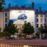 Vue de face de nuit du dispositif Volkswagen illuminé qui finance les travaux de façade sur la place Bellecour à Lyon.
