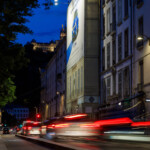Plan resserré de nuit sur l'affichage Volkswagen finançant les travaux de façade, avec la basilique de Fourvière en arrière-plan.