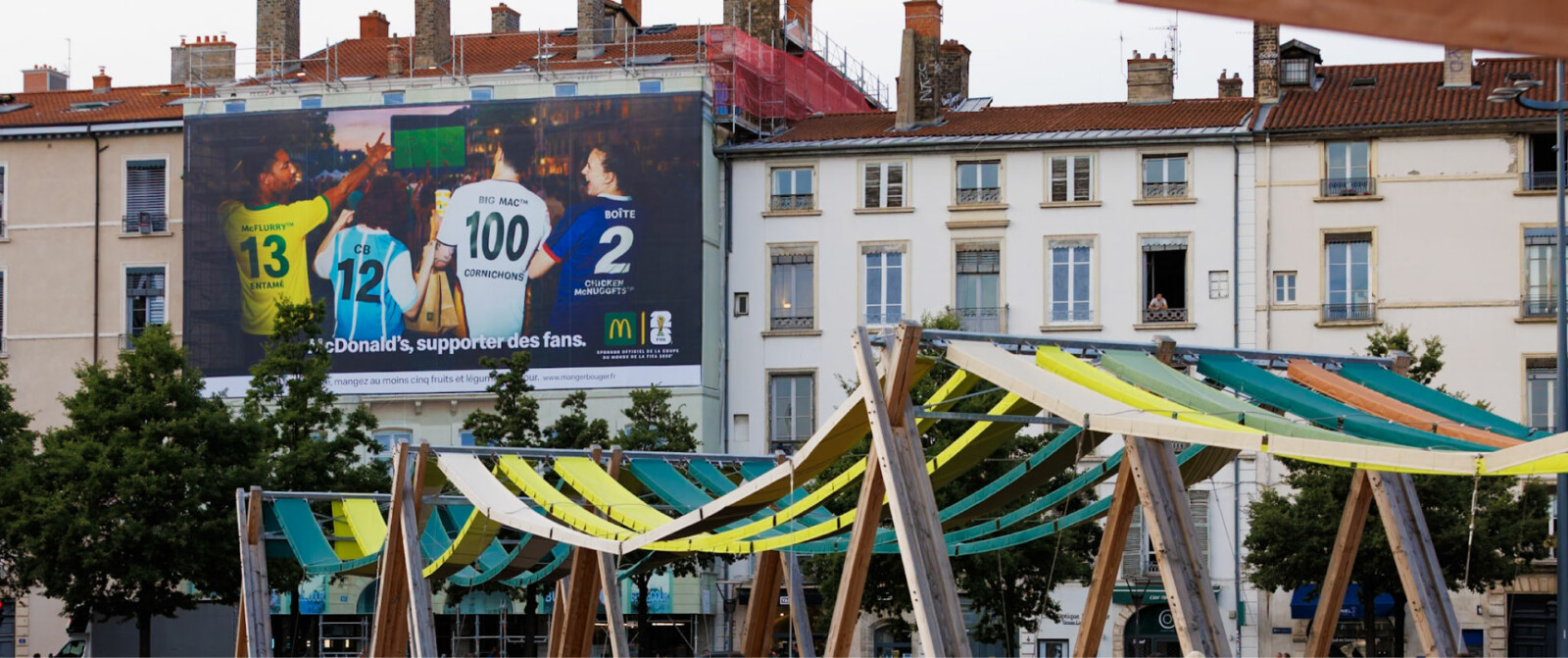 Vue lointaine de jour de face illustrant l'intégration urbaine parfaite de cette campagne grand format au cœur de Lyon, sur la place Bellecour.