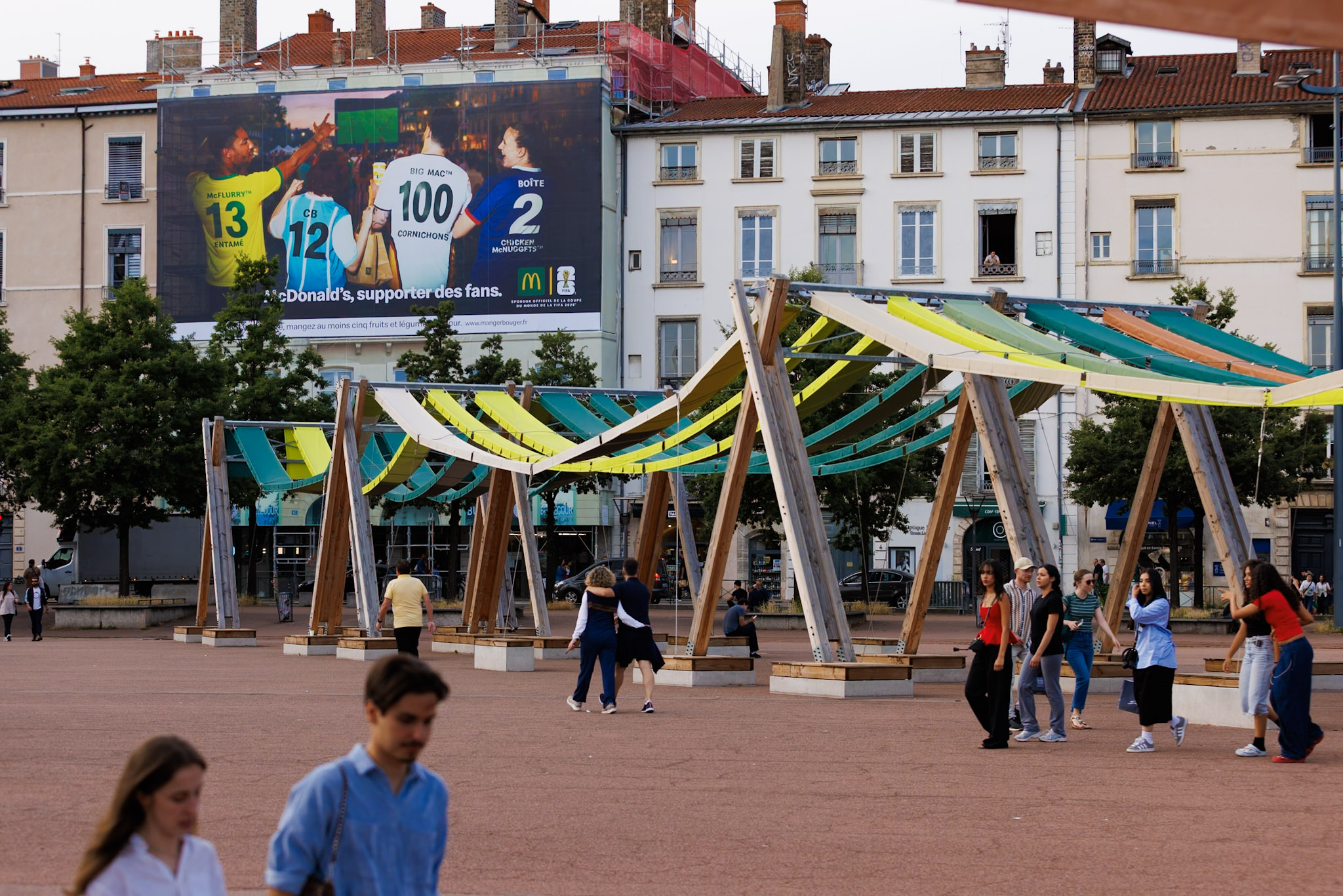 Vue lointaine de jour de face illustrant l'intégration urbaine parfaite de cette campagne grand format au cœur de Lyon, sur la place Bellecour.
