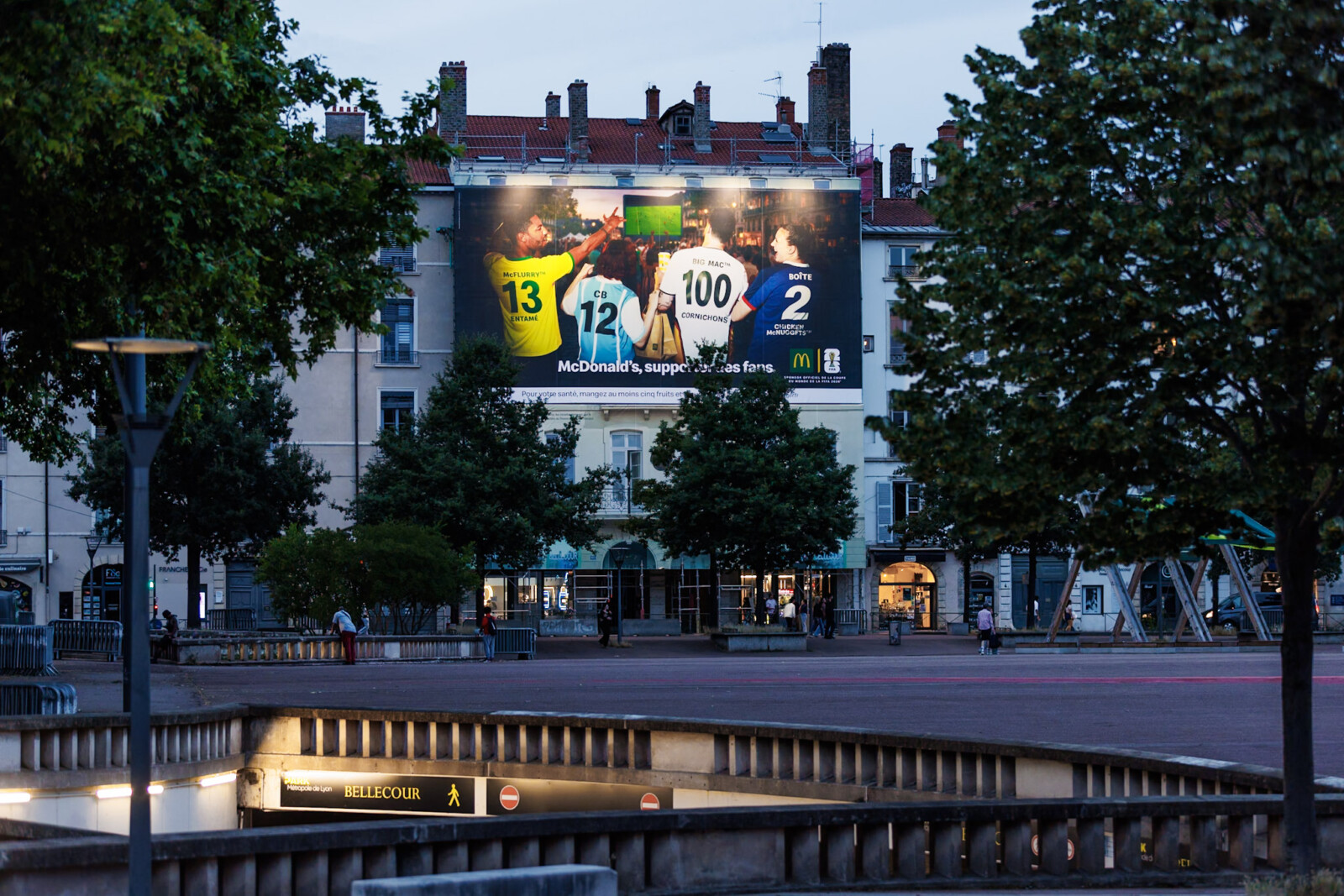 Superbe vue lointaine de nuit de face mettant en lumière la campagne grand format McDonald's sur la place Bellecour à Lyon.