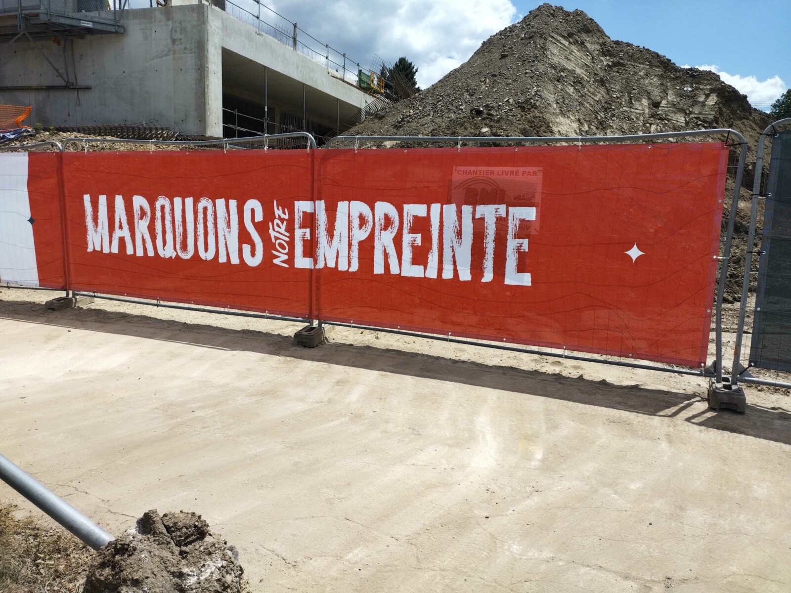 Palissade de chantier en toile rouge avec impression texte "Marquons notre empreinte" pour communication BTP.