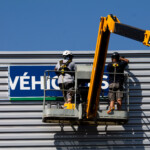 Techniciens installant le panneau d'enseigne véhicule sur nacelle à Dijon