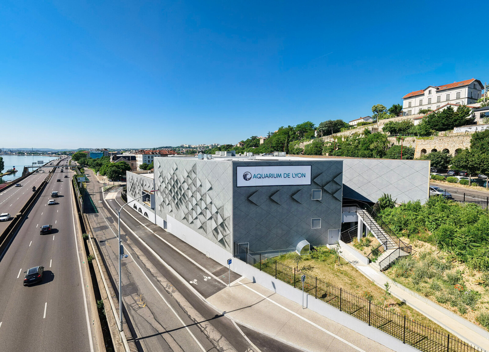 Vue aérienne de l'enveloppe du bâtiment de l'Aquarium de Lyon intégrant une enseigne grand format au bord de l'autoroute.