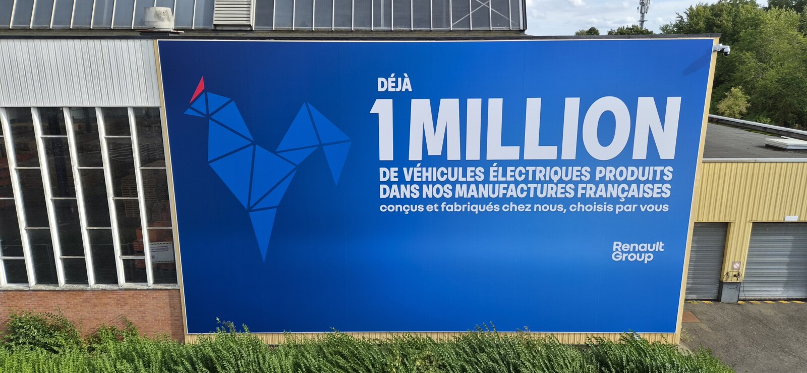 Gros plan sur la pose d'une toile tendue grand format sur le bardage métallique d'un bâtiment industriel.